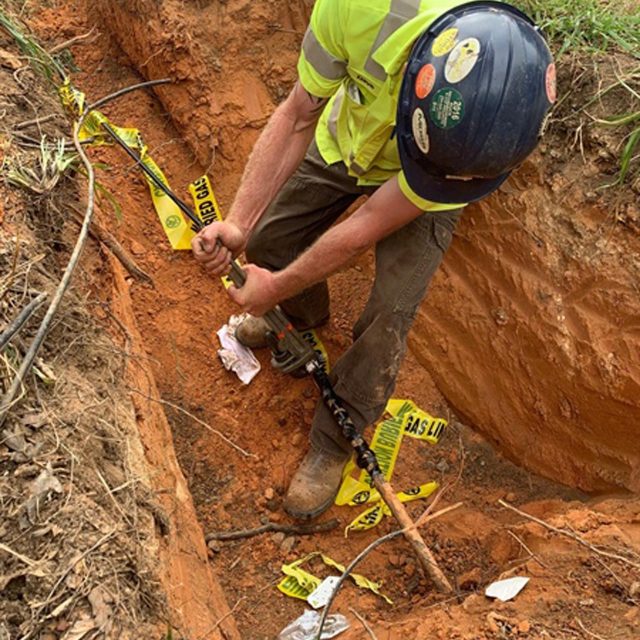 HALL Contracting Corporation employee wearing black helmet dig a hole in the ground