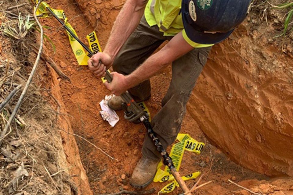 HALL Contracting Corporation employee wearing black helmet dig a hole in the ground