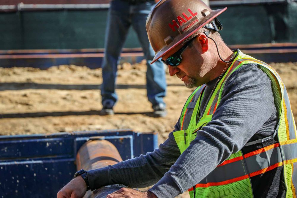 HALL employee wearing yellow vest and brown and red helmet works on job site